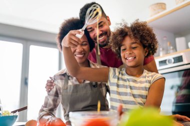 Coşkulu Afro-Amerikalı çocuklu genç bir aile evde birlikte yemek pişiriyor, mutlu gülümseyen ebeveynler hafta sonları mutfakta çocukla eğleniyor.