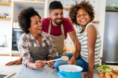 Coşkulu Afro-Amerikalı çocuklu genç bir aile evde birlikte yemek pişiriyor, mutlu gülümseyen ebeveynler hafta sonları mutfakta çocukla eğleniyor.