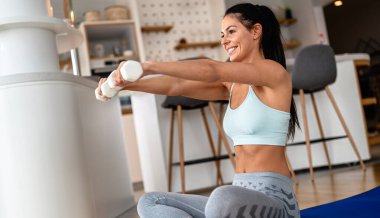 Kararlı kadın evde kilo veriyor ve halterlerle egzersiz yapıyor. Spor ve eğlence konsepti. Spor giyimli güzel bir kadın ellerinde beyaz halterlerle..