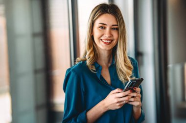 Genç, mutlu, zarif, profesyonel bir iş kadını. Yönetici ofisinde cep telefonu kullanıyor, cep telefonu tutuyor ve çalışıyor..