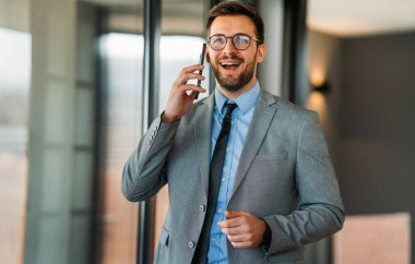 Ofiste cep telefonu kullanan mutlu orta yaşlı iş adamı yöneticisi. Gülümseyen iş adamı CEO yatırımcı elinde akıllı telefonuyla şirket ofisinde duruyor..