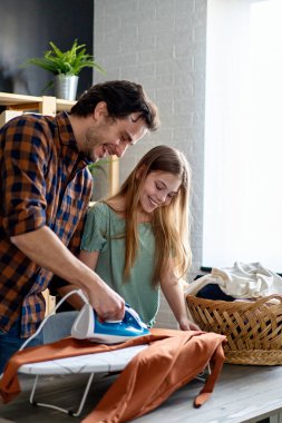 Mutlu bir baba ve kızı evde ev işleri yapıyor ve birlikte ütü yapıyor. İnsanların mutluluk kavramı.