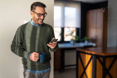 Elektronik bankacılık için akıllı telefon ve dizüstü bilgisayar kullanan, rezervasyon yapan, online alışveriş yapan ve evde vakit geçirirken ödeme yapan şık giyimli bir adam..