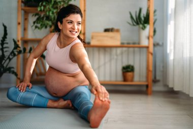 Evde çalışan hamile bir kadının portresi. Hamile kadın evde yoga yapıyor. Doğum öncesi kasıklar gerilir. Hamilelik yogası ve fitness.