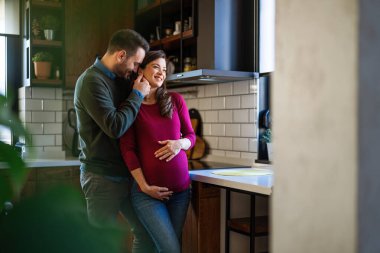 Aşırı mutlu hamile bir eş kocaya sarılıyor, son üç aylık dönemde evde romantik anların tadını çıkarıyor. Hamilelik, yeni aile, mutluluk kavramı.