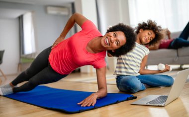 Güzel siyah anne ve genç kız birlikte yoga dersi alıyorlar, dizüstü bilgisayarın önünde spor yapıyorlar.