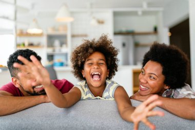 Happy biracial girl smiling with young multiracial parents enjoy weekend at home together, overjoyed multiethnic daughter play with loving mom and dad clipart