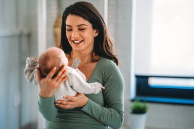 Sevgi dolu anne yeni doğmuş bebeğini evde taşıyor. Mutlu bir annenin parlak portresi. Elinde uyuyan bir bebeği tutuyor..