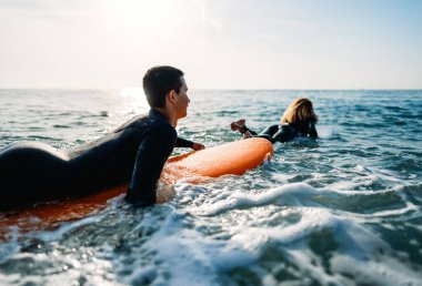 Sörf tahtası olan iki mutlu genç sörfçü gün batımında dalgalara vurmaya hazırlanıyor. Aktif spor yaşam tarzı tatil kavramı