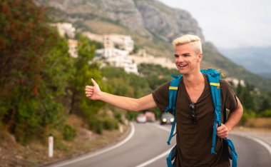 Yalnız seyahat etme kavramı. Güneşli bir yaz gününde yolda otostop çeken genç beyaz bir adam. Sırt çantalı hippi, dağlarda arabayı durdurmaya çalışıyor..