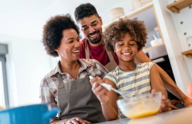 Coşkulu Afro-Amerikalı çocuklu genç bir aile evde birlikte yemek pişiriyor, mutlu gülümseyen ebeveynler hafta sonları mutfakta çocukla eğleniyor.