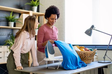 Güzel siyah kadın ve çocuk yardımcıları evde ütü yaparken eğleniyor ve gülümsüyorlar..