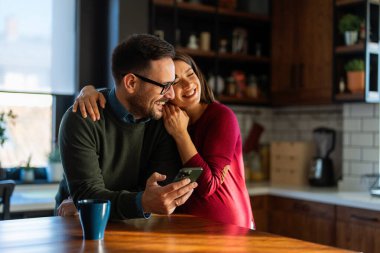 Hamilelik, teknoloji ve insan kavramı. Mutlu adam ve evde akıllı telefonları olan hamile karısı. Yeni mutlu aile.