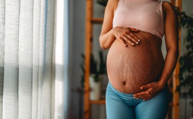 Güzel bir gülümsemesi olan, karnına el ele tutuşan, hamileliğinin son üç ayının tadını çıkaran çekici hamile bir kadın..