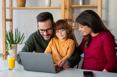 Çocuklu mutlu bir aile birlikte dizüstü bilgisayar kullanarak eğleniyor, ebeveynler ve çocuklar evde gülüyor bilgisayarla komik bir internet videosu izliyor, online arama yapıyor.