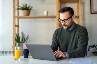 Tatmin olmuş yakışıklı adam dizüstü bilgisayarda yazıyor, internetten e-posta yazıyor, uzaktan çalışıyor ya da evde bilgisayar başında çalışıyor.