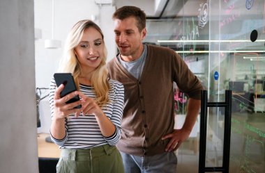 Erkek bir iş arkadaşıyla tartışıyor, akıllı bir telefona bakıyor ve ofiste birlikte çalışıyor.