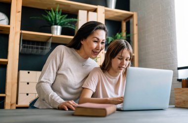 Mutlu genç Asyalı bekar anne evde eğitim görürken dizüstü bilgisayar kullanarak tatlı bir kızla ders çalışıyor.
