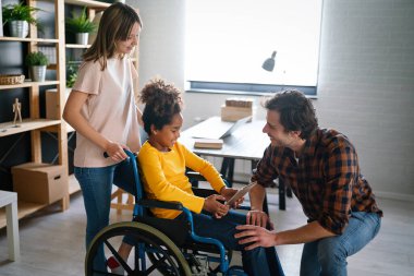 Tekerlekli sandalyedeki engelli çocukla birlikte evde eğlenen çok ırklı mutlu bir aile.