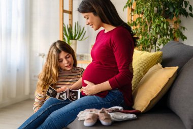 Heartwarming family moment as expectant mom and daughter joyfully browse through newborn babys clothes, eagerly anticipating the arrival of a new family member