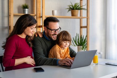 Çocuklu mutlu bir aile birlikte dizüstü bilgisayar kullanarak eğleniyor, ebeveynler ve çocuklar evde gülüyor bilgisayarla komik bir internet videosu izliyor, online arama yapıyor.