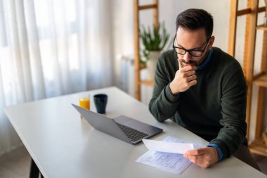Doymuş modern adam elektronik bankacılık için dizüstü bilgisayar kullanıyor, rezervasyon yaptırıyor, online alışveriş yapıyor ve evde vakit geçirirken ödeme yapıyor..