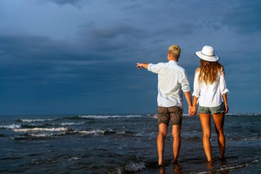 Kumsalda yürüyen bir çift. Genç mutlu ırklar arası çift kumsalda yürüyor gülümsüyor, yaz tatilinin tadını çıkarıyor, balayına çıkıyor.