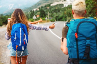 Neşeli ırklar arası arkadaşlar yol kenarında pankartlarla duruyorlar, otostop çekiyorlar, yaz tatilinde arabayı durduruyorlar. Turizm, birlikte seyahat, özgürlük ve arkadaşlık kavramı