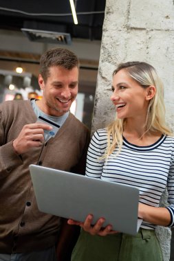 Genç çift evdeki internet sitesinden online alışveriş için kredi kartını kullanıyor. Bilgisayarı kullanarak ecommerce sitesinden alırken bankamatik kartı tutan mutlu çift..