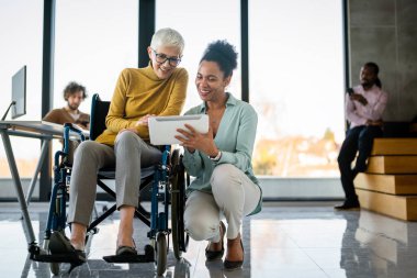 Tekerlekli sandalyedeki engelli kadın bilgisayara bakıyor, ırklar arası projeyi tartışıyor. Katılım, eşitlik mutlu iş insanları konsepti.