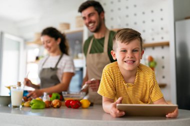 Mutfakta çocuklu mutlu bir aile birlikte modern tablet kullanarak eğleniyor, gülümseyen ebeveynler çocuklarla birlikte hafta sonunun keyfini çıkarıyor evde bilgisayardan gülen videolar izliyorlar.