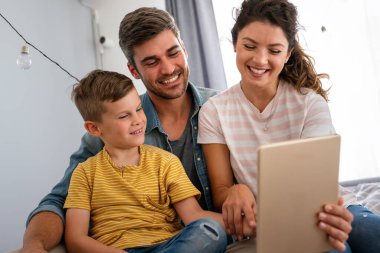 Çocuklu mutlu bir aile tablet bilgisayar kullanarak eğleniyor, ebeveynler ve çocuklar gülüyor evde bilgisayarla komik internet videoları izleyip, online arama yapıyorlar.