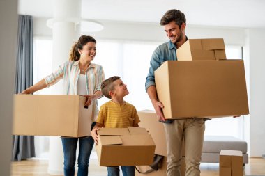 Taşındığı gün yeni evde karton kutuları olan mutlu bir aile. İpotek, aile ve gayrimenkul konsepti, mutlu anne, baba ve çocuk kutuları yeni eve taşınıyor.