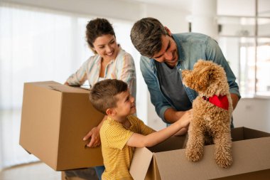 Taşındığı gün yeni evde karton kutuları olan mutlu bir aile. İpotek, aile ve gayrimenkul konsepti, mutlu anne, baba ve çocuk kutuları yeni eve taşınıyor.