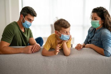 Aile, koronavirüse karşı maske takıyor, kirlilik, hastalık ve evde kalıyor. Virüsü, gribi ve kirliliği önlemek için koruyucu maske takan üzgün aile.