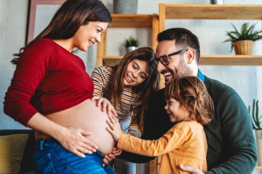 Sevgi dolu koca ve çocuklar hamile annelere sarılıyorlar, karnına dokunuyorlar. Mutlu, heyecanlı bir aile bebek bekliyor, yeni aile üyeleri.