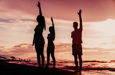 Sağlıklı yaşam tarzını uygulayan bir grup insan, plajda yoga. Yoga pozisyonunda denge, açık havada spor, mutluluk kavramı.