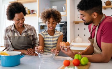 Coşkulu Afro-Amerikalı çocuklu genç bir aile evde birlikte yemek pişiriyor, mutlu gülümseyen ebeveynler hafta sonları mutfakta çocukla eğleniyor.