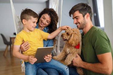 Çocuklu mutlu bir aile tablet bilgisayar kullanarak eğleniyor, ebeveynler ve çocuklar gülüyor evde bilgisayarla komik internet videoları izleyip, online arama yapıyorlar.
