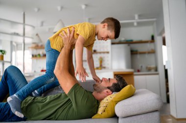 Ebeveyn ve çocuk arkadaş oluyor. Neşeli baba ve oğul, eğlenceli, neşeli genç baba kanepede uzanıyor, heyecanlı küçük oğlunu kaldırıyor, evde birlikte vakit geçiriyorlar. Bekar baba kavramı