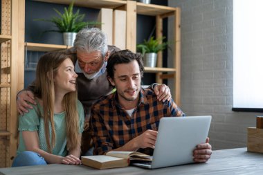 Mutlu genç baba, büyükbaba evde eğitim görürken dizüstü bilgisayar kullanıyor.