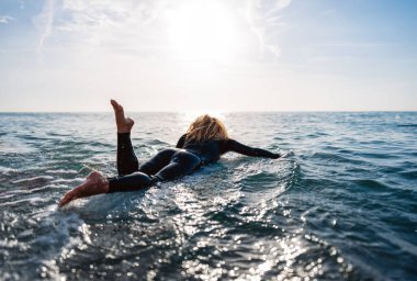 Genç mutlu bir kadının portresi, sahilde sörf yapmak ve eğlenmek, özgürlük konsepti. Mutlu genç bayan sörfçü, güneş ışığı ve macera denizi