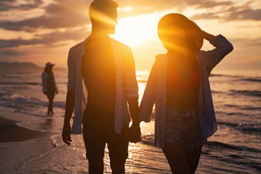 Kumsalda birlikte yürüyen tatilci çift birbirine sarılıyor. Mutlu ırklar arası genç çift yaz tatilinde balayının tadını çıkarıyor.