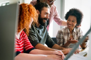 Mixed team of software engineers brainstorming ideas for new code library in front of computer screens compiling algorithms. Diverse app developers collaborating on group project in it agency office.