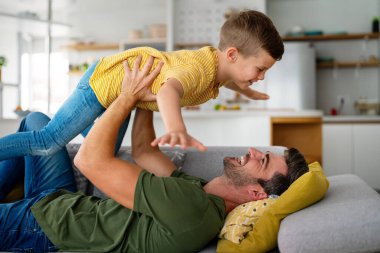 Neşeli, genç bir baba kanepeye uzanmış, heyecanlı, küçük bir çocuğu kaldırıyor. Uzun boylu, kaygısız iki nesildir aile oturma odasında eğleniyor..