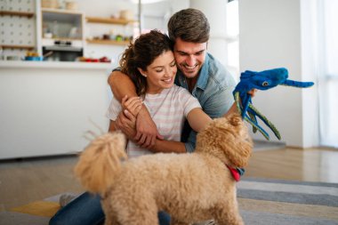 Evcil hayvanlarıyla oturma odasında vakit geçiren ırklar arası evli bir çift. Mutlu çift köpekle oynuyor, evde yerde eğleniyor.