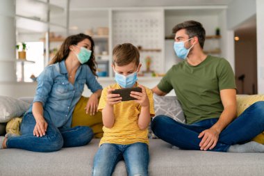 Aile, koronavirüse karşı maske takıyor, kirlilik, hastalık ve evde kalıyor. Virüsü, gribi ve kirliliği önlemek için koruyucu maske takan üzgün aile.