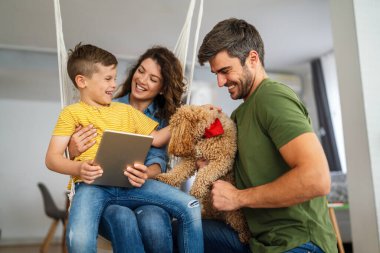 Çocuklu mutlu bir aile tablet bilgisayar kullanarak eğleniyor, ebeveynler ve çocuklar gülüyor dijital cihazla evde dinleniyorlar, komik internet videoları izliyorlar, online arama yapıyorlar.