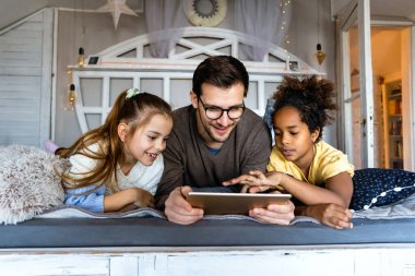 Mutlu çoklu etnik çeşitlilikte bir aile, baba ve çocuklar evde birlikte zaman geçiriyorlar ve dijital aletler kullanıyorlar..
