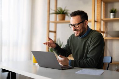 Kendine güvenen iş adamı yönetici koçu. Günlük kıyafetlerini giyip dizüstü bilgisayar kullanıyor, sanal görüşme yapıyor, profesyonel eğitim pazarlığı yapıyor, uzaktan kumandayı evden yapıyor..